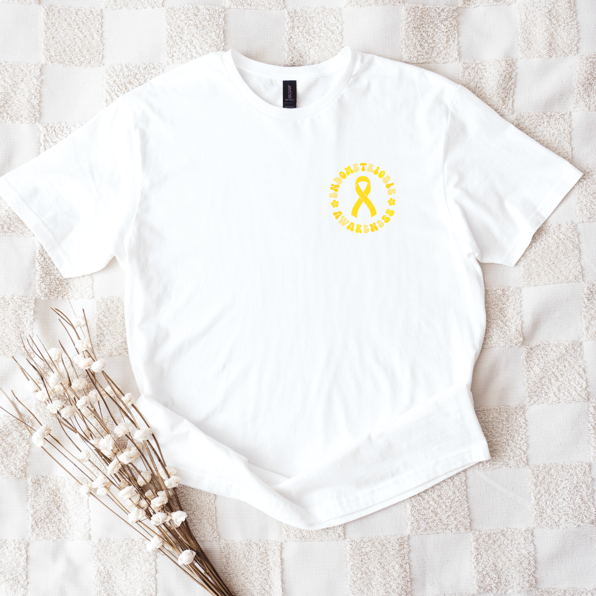 Maddy and George Designs white cotton tee flatlay with small yellow ribbon logo on chest Endometriosis Awareness Shirt .