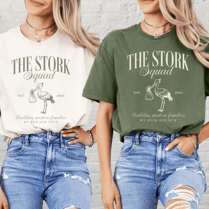 Two women wearing Matching Surrogacy Announcement Tee The Stork Squad print in cream and olive with distressed jeans