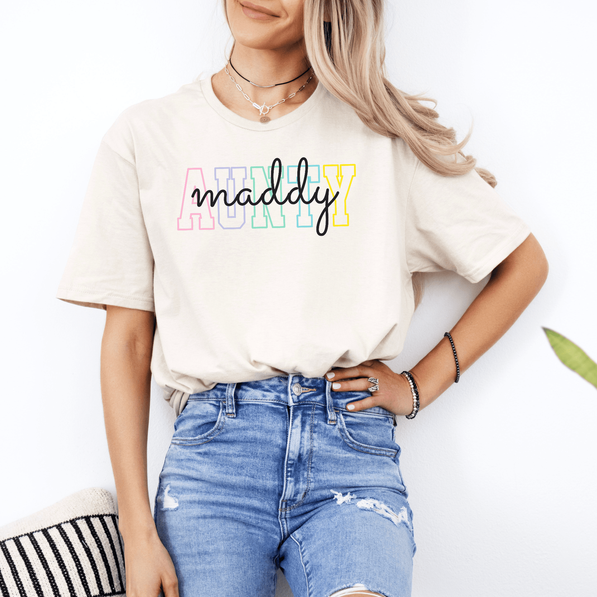Woman wearing beige Maddy and George Designs Custom Aunty Shirt with pastel block letters and script logo