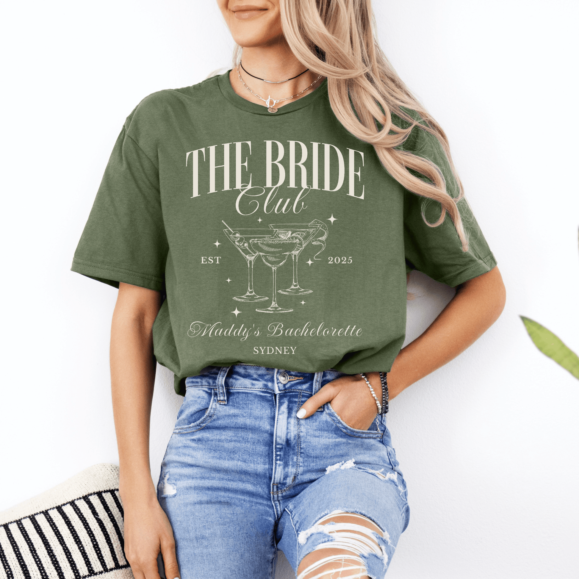 Woman wearing olive green Custom Bachelorette Party Tee by Maddy and George Designs reading The Bride Club with martini glasses