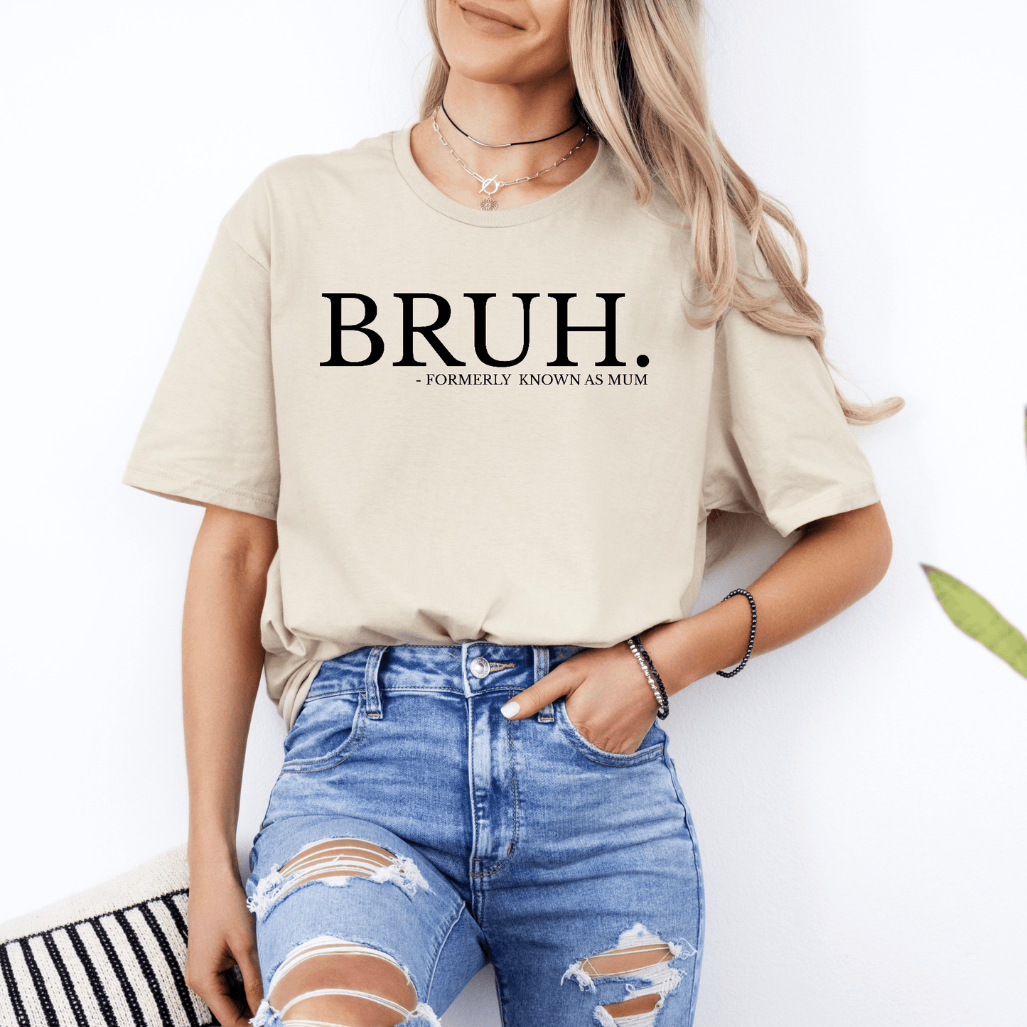 Woman wearing beige tee with bold slogan Bruh. Formerly Known as Mum Shirt by Maddy and George Designs paired with ripped jeans
