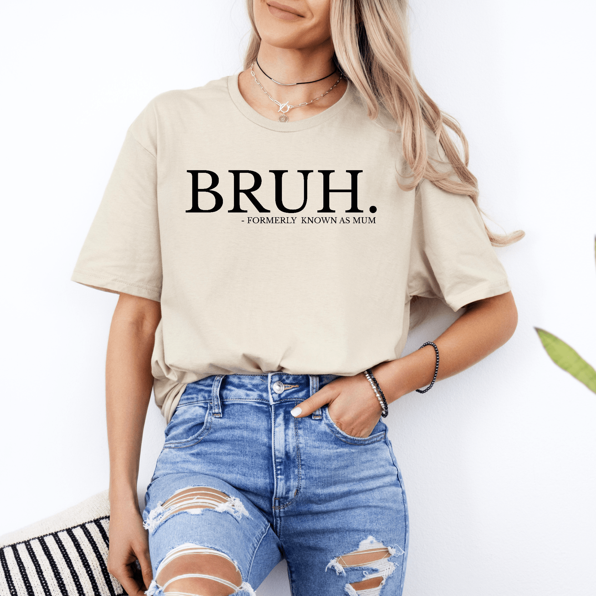 Woman wearing beige tee with bold slogan Bruh. Formerly Known as Mum Shirt by Maddy and George Designs paired with ripped jeans