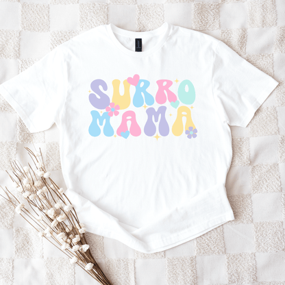 White t shirt with pastel bubble letters and flowers reading Surro Mama laid flat on blanket Cute Surrogate Mama Shirt
