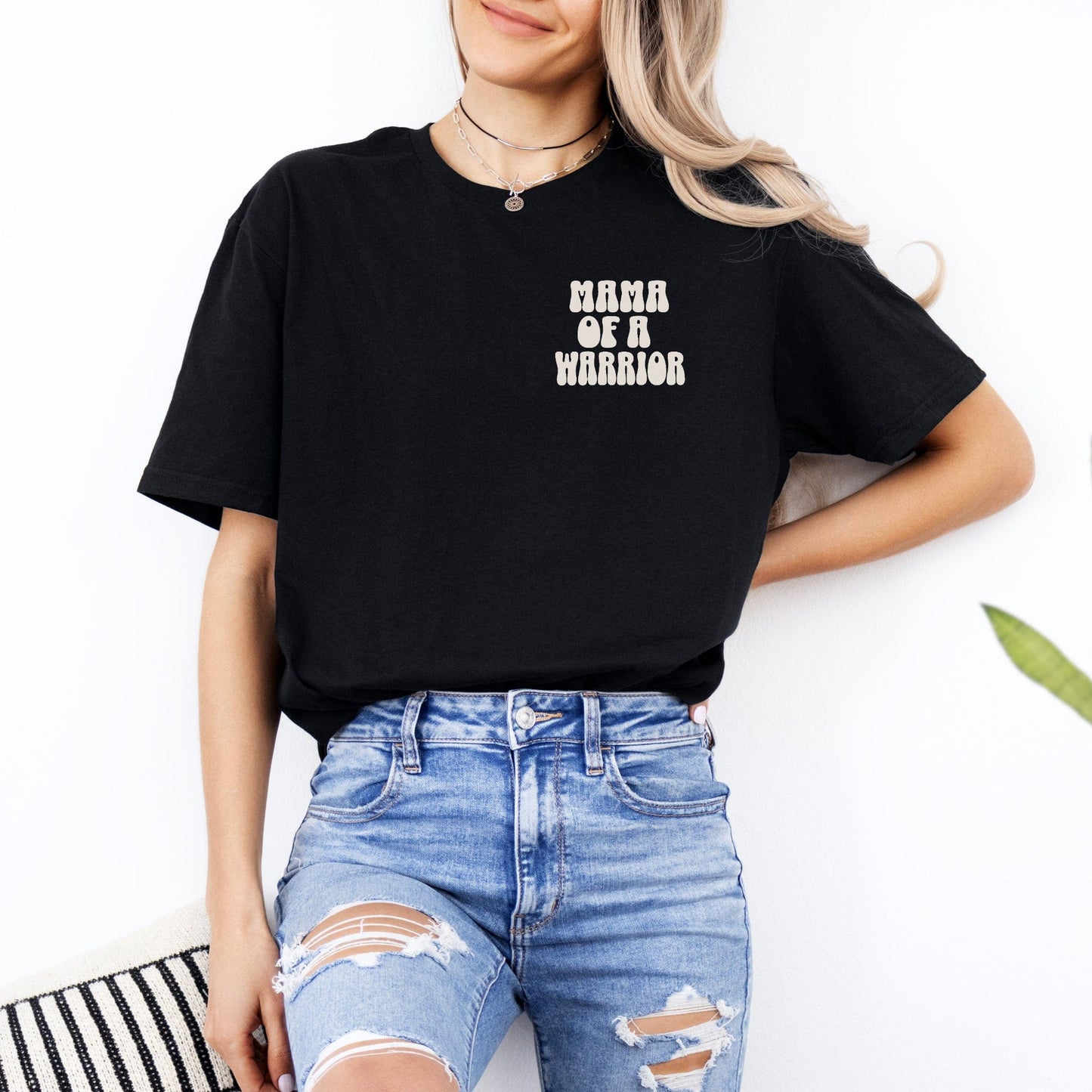 Woman wearing Mama of a Warrior Club Shirt black tee with small chest print paired with ripped blue jeans