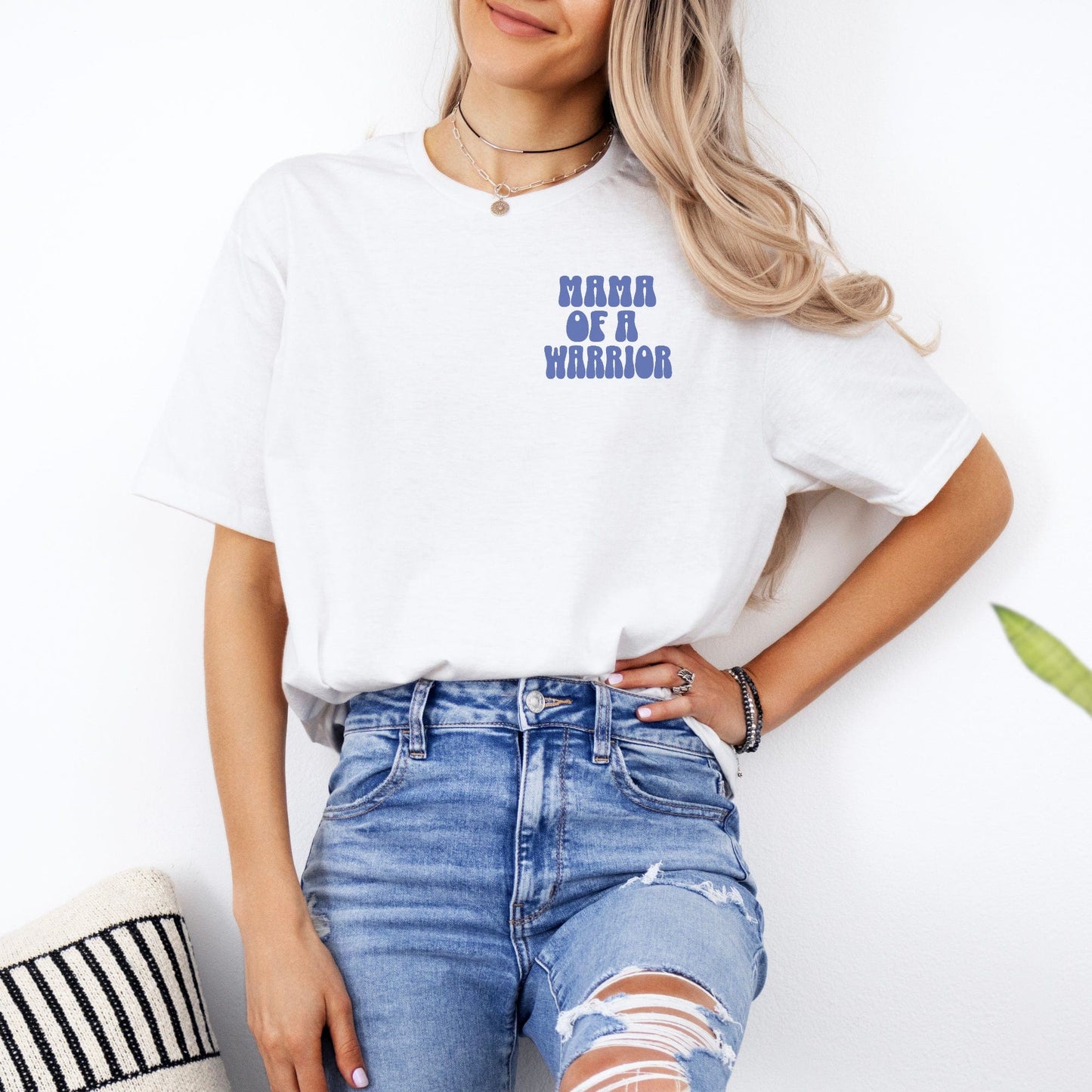 Maddy and George Designs white tee worn by woman featuring blue chest print Mama of a Warrior Club Shirt supportive parent apparel