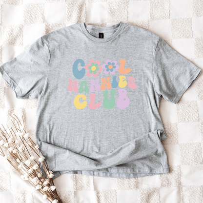 Gray unisex t shirt laid flat on blanket with pastel retro bubble lettering and flower graphics Cool Nannies Club Shirt