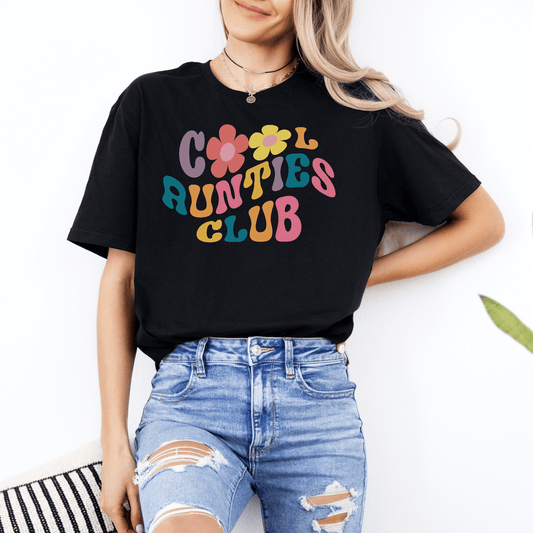 Woman wearing black Retro Cool Aunties Club Shirt with colorful 1970s flower lettering paired with ripped jeans