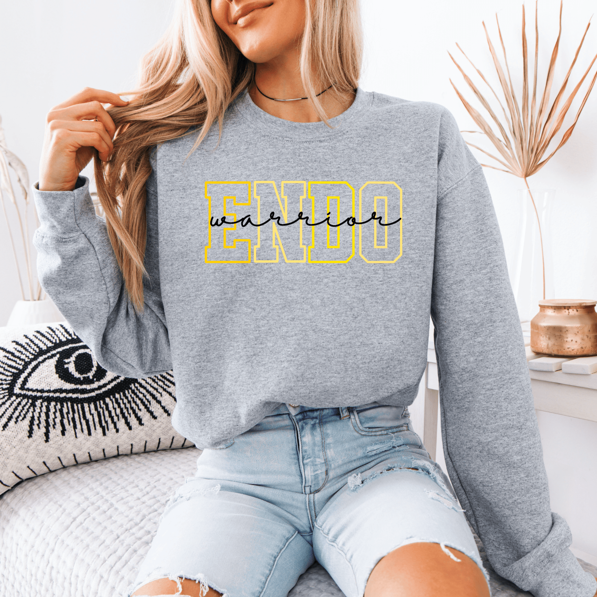 Woman wearing gray crewneck sweatshirt with yellow outlined ENDO letters and script, Endometriosis Warrior Sweatshirt .
