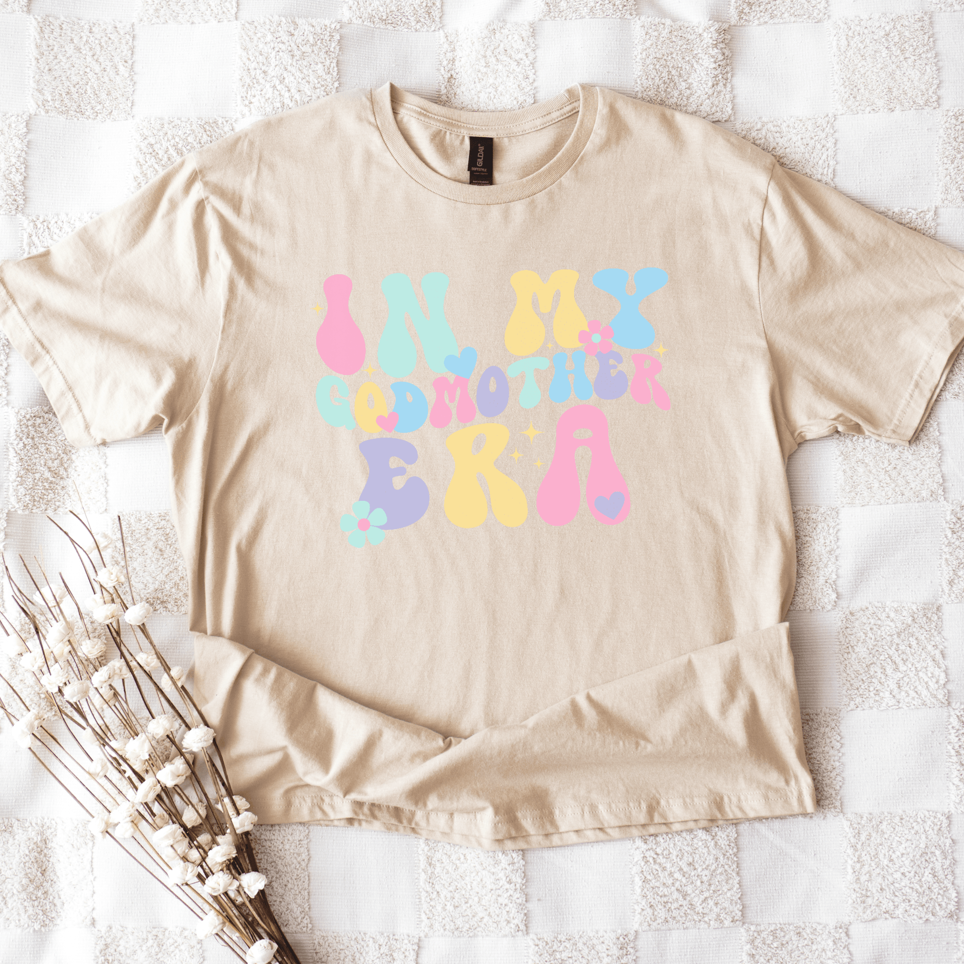 Beige short sleeve cotton tee flat lay with pastel retro bubble lettering reading In My Godmother Era Godmother Announcement Shirt