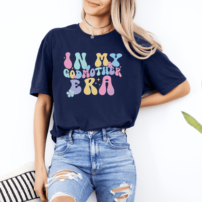 Woman wearing navy Godmother Announcement Shirt with colorful retro In My Godmother Era design tucked into jeans