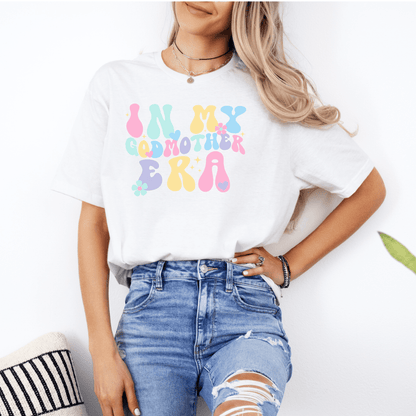 Woman wearing Maddy and George Designs Godmother Announcement Shirt white tee with pastel retro bubble text for pregnancy reveal