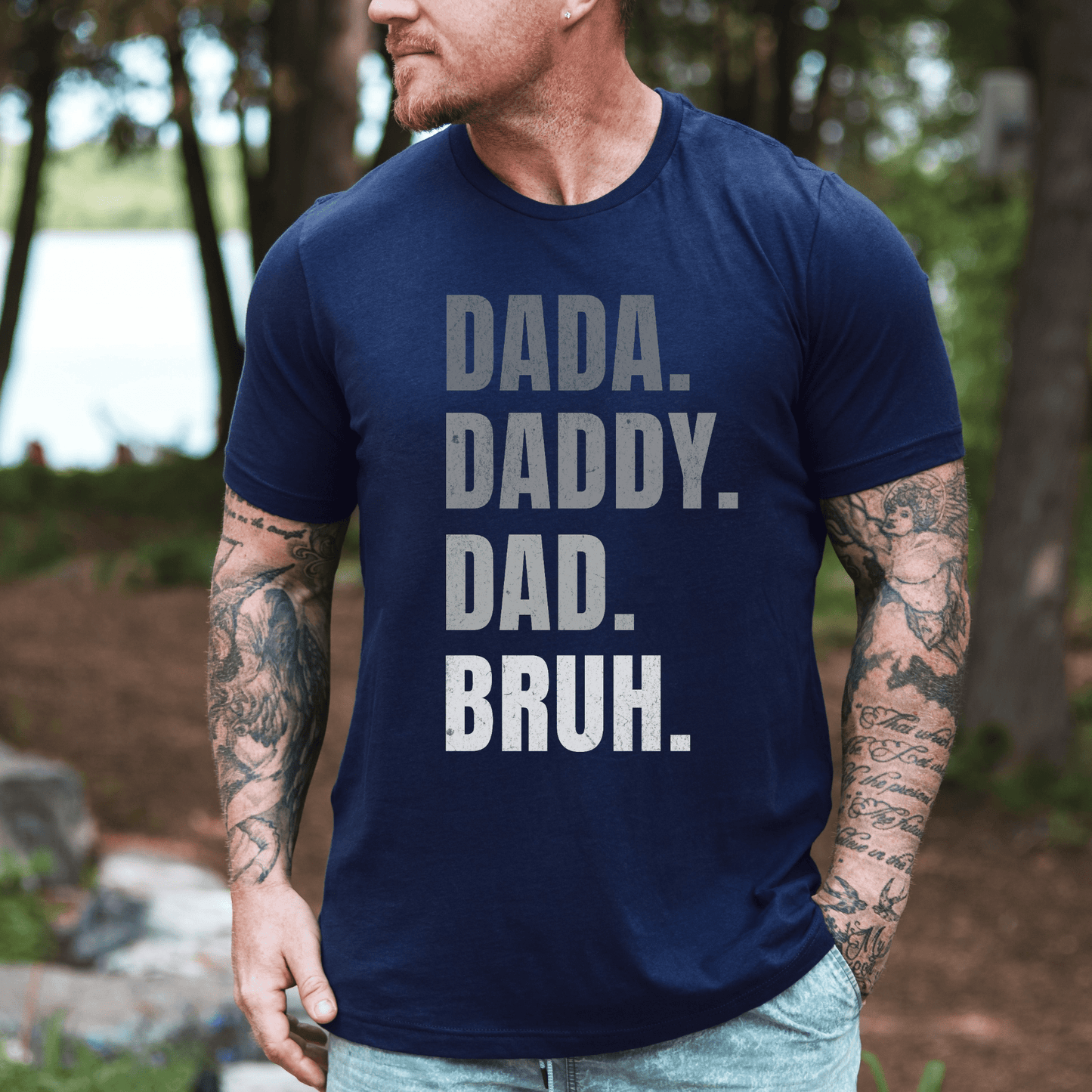 Dada. Daddy. Dad. Bruh Shirt printed on navy tee worn by tattooed man outdoors lakeside
