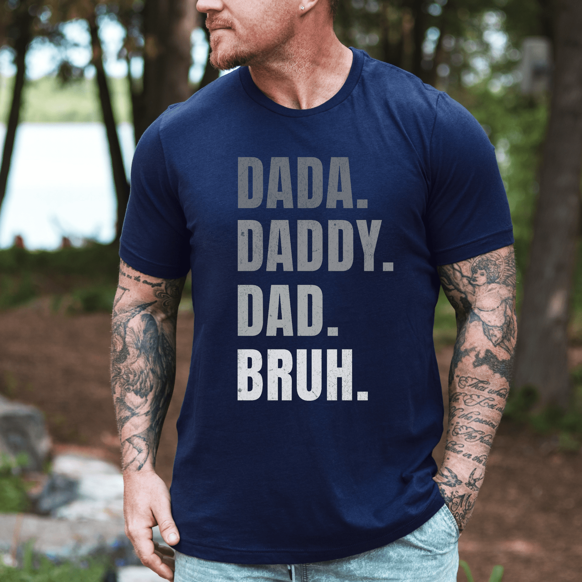 Dada. Daddy. Dad. Bruh Shirt printed on navy tee worn by tattooed man outdoors lakeside