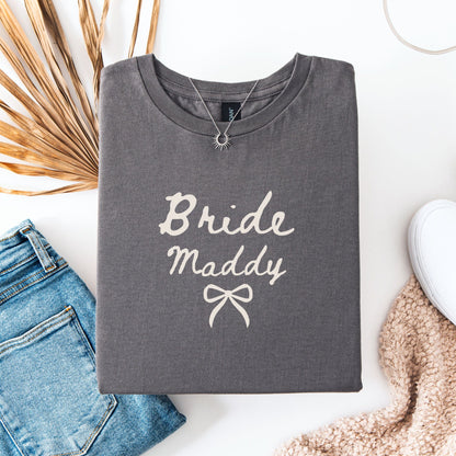 Custom Bride T-Shirt gray folded with Bride Maddy script and bow flat lay with jeans necklace and sneakers