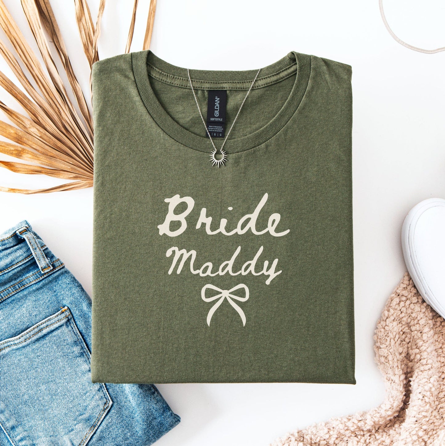 Olive green Custom Bride T-Shirt with Bride Maddy script and bow styled flatlay with jeans sneaker and necklace