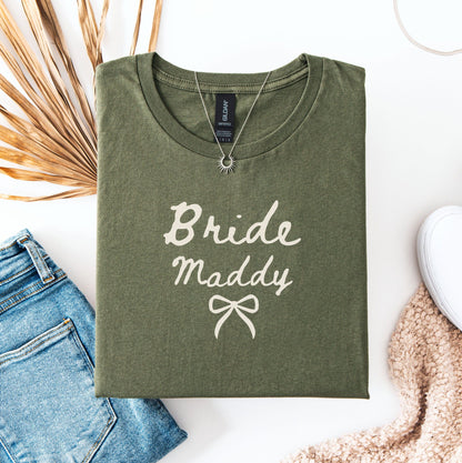 Olive green Custom Bride T-Shirt with Bride Maddy script and bow styled flatlay with jeans sneaker and necklace