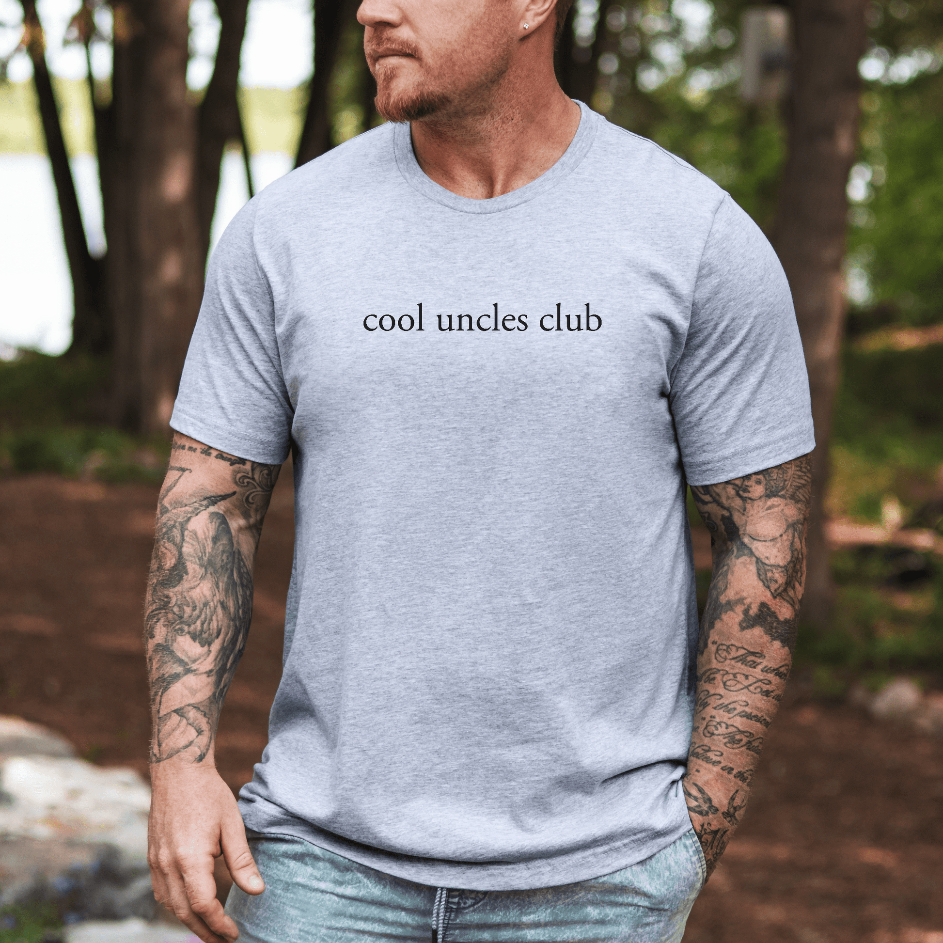 Minimalist Cool Uncles Club Shirt light gray tee with black cool uncles club text worn by tattooed man outdoors