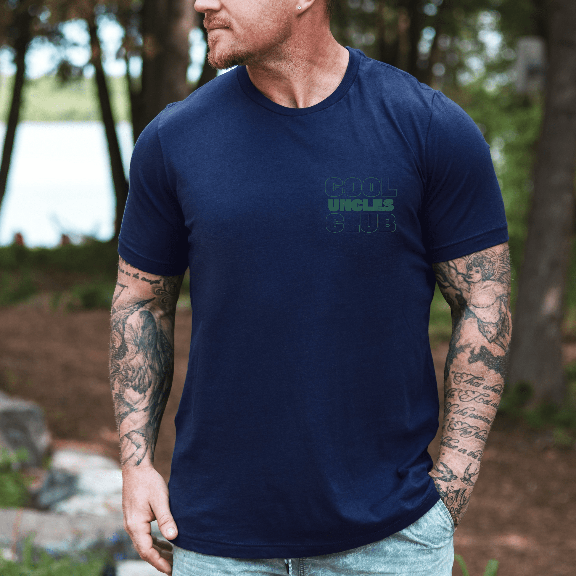 Maddy and George Designs model wearing navy cool uncle shirt with small chest logo short sleeves tattoos outdoors