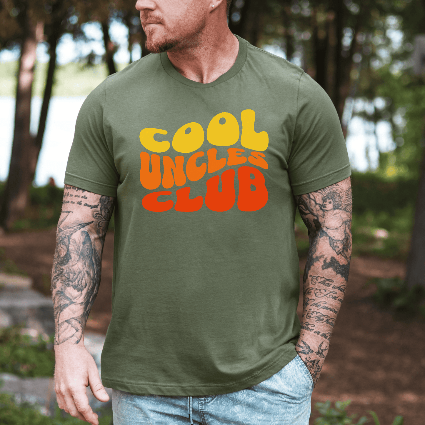 Cool Uncles Club Shirt olive green tee with retro yellow and orange bubble text worn by tattooed man outdoors