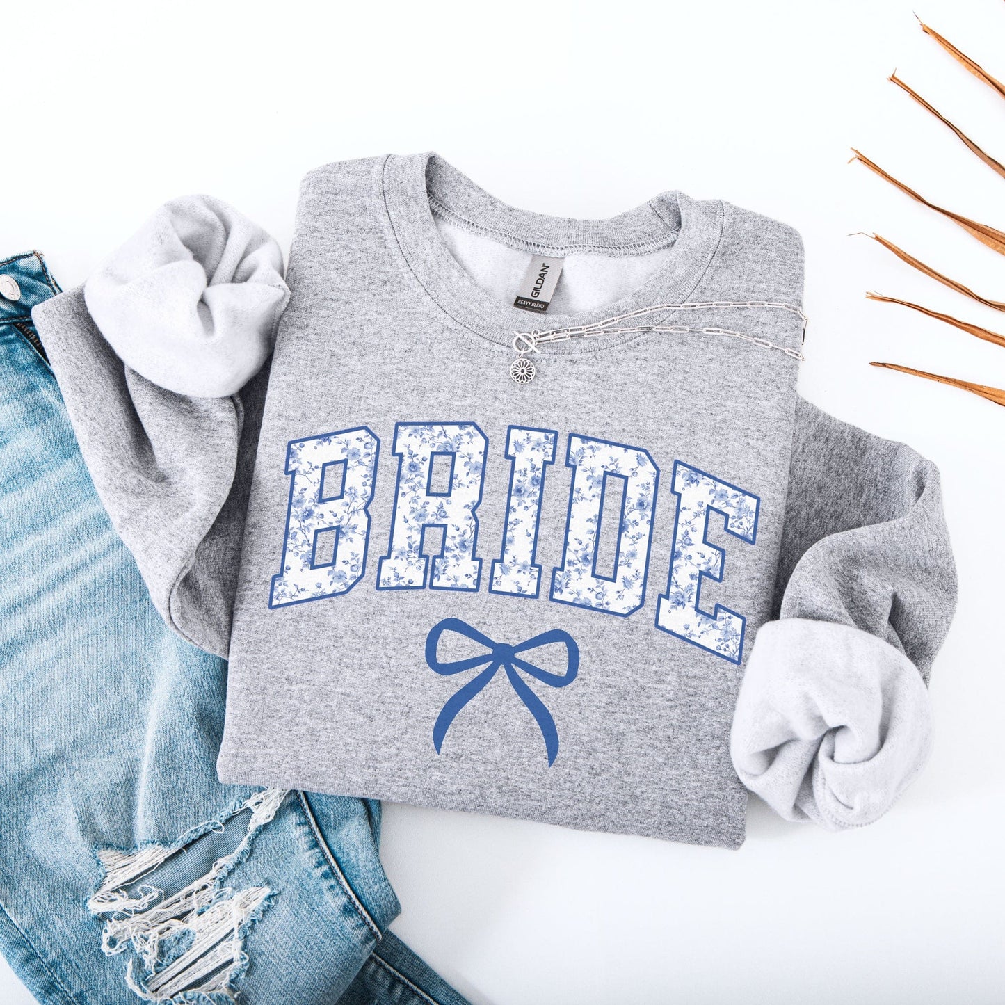 Chinoiserie Bride Sweatshirt grey folded with blue floral BRIDE letters and bow styled with ripped jeans and necklace