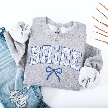 Chinoiserie Bride Sweatshirt grey folded with blue floral BRIDE letters and bow styled with ripped jeans and necklace