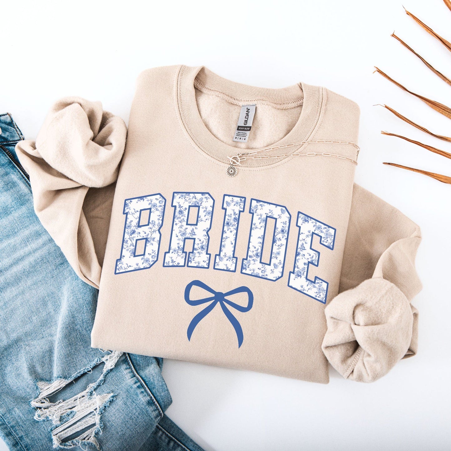 Chinoiserie Bride Sweatshirt beige folded flatlay with blue floral BRIDE lettering bow and distressed jeans